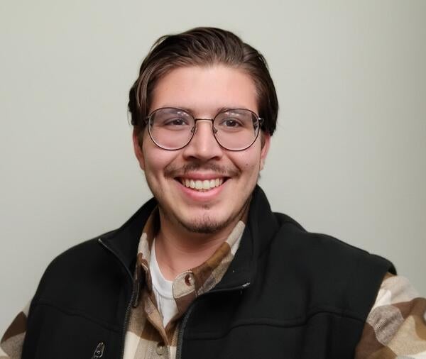 a man with a vest and glasses in front of a white wall
